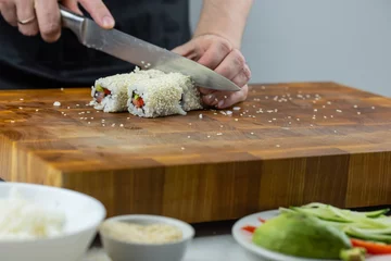 Foto op Canvas Closeup of chef hands preparing japanese food. Professional chef making sushi at restaurant. Man hands making traditional asian sushi rolls on cutting board. © strigana