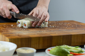 Closeup of chef hands preparing japanese food. Professional chef making sushi at restaurant. Man hands making traditional asian sushi rolls on cutting board.