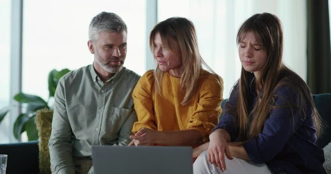 Young daughter showing photograph of her boyfriend to parents getting confused with their reaction. Mother laughing and looking on laptop monitor. Humor concept.
