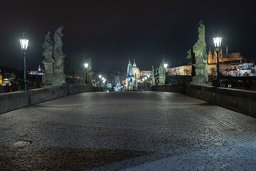 Obraz premium lit lanterns and illuminated statues and sidewalk with cobblestones on an empty charles bridge at night during a lockdown