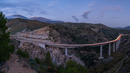 Fototapeta na wymiar Long exposure of a long viaduct between mountains and with Sierra Nevada in the background.