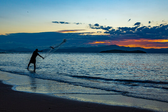 Our daily fish. Silhouette of a fisherman throwing the fishing net, called "tarrafa" on the Sambaqui beach in Florianópolis.