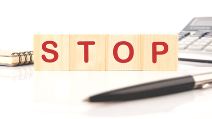 Four wooden cubes with the word Stop On a white background next to a pen, calculator and notepad