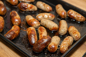 A trey of cooking cooked backed mini sausages