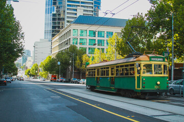 Fototapeta premium Vintage tram in Melbourne, Australia, rolling down the track in a modern district on a sunny day.