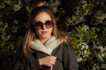 beautiful girl on the street in spring against the background of greenery and flowers in a jacket and sunglasses