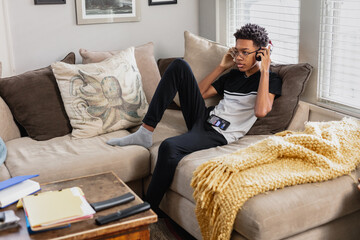 Black teen boy puts on headphones to listen to music at home, relaxed
