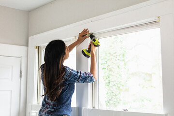 Indian woman using drill power tool to install blinds, DIY home improvement project