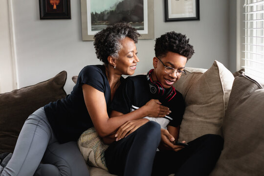 Black mother and son laughing together on couch, loving moment