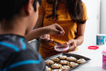 Indian mother and son decorating fresh baked cookies in the kitchen