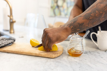 Black man with tattoos slices fruit for tea drink