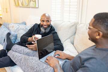 Black gay men have conversations on couch at home