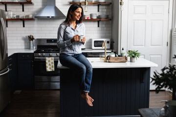 Young Indian woman sitting on kitchen counter, with tea drink