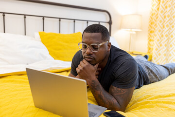 Black man working from home on laptop in bed
