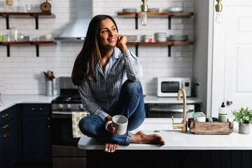 Young Indian woman sitting on kitchen counter, with tea drink