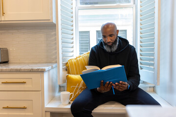 Black man, cozy, reading book in nook at home