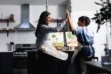 Indian mother and son high-five after completing art project for school, at home