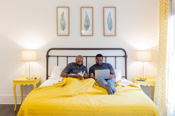 Black same gender couple working and reading in bed