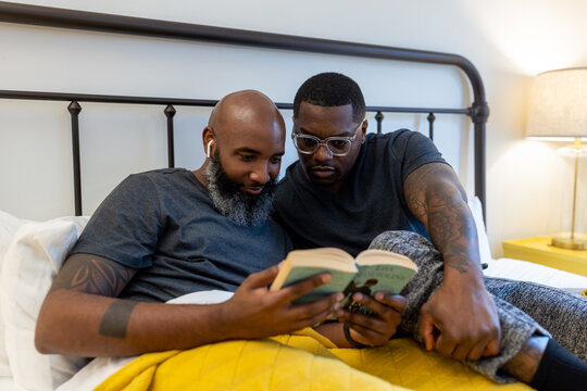African American gay couple working and reading in bed at home, LGBTQ love