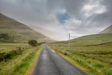 Fototapeta na wymiar Small narrow asphalt road into mountains, Connemara, Ireland. Low cloudy sky. Nature background. Nobody. Rural area