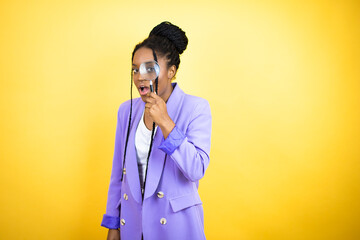 Young african american business woman surprised looking through a magnifying glass