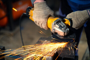 Locksmith in special clothes and goggles works in production. Metal processing with angle grinder. Sparks in metalworking