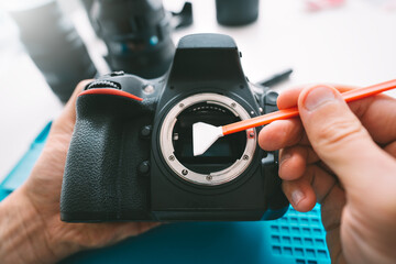 Photographer cleaning matrix of his camera with camera sensor cleaner or cleaning swab. Photography equipment care