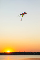 Colorful kite flying near river at sunset