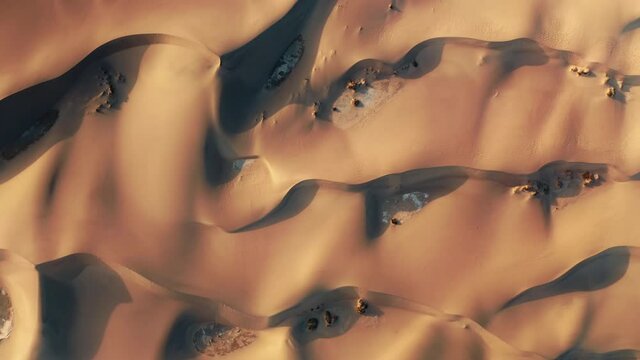 Beautiful aerial background of wild nature scenic landscape. 4K top down view on the abstract wavy pattern on the sand desert surface painted by the sunset light and deep shadows on the high dunes