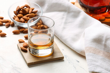 Glass of almond liquor and nuts on light background