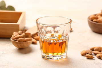 Glass of almond liquor and nuts on light background, closeup