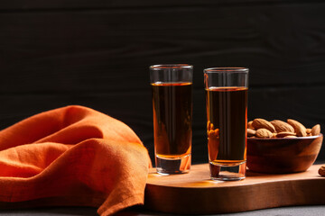 Board with glasses of almond liquor and nuts on dark background