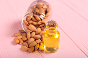 Bottle of almond oil and nuts on color wooden background