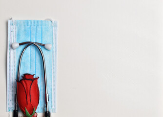Fototapeta na wymiar Medical equipment and a red rose placed on a white surface while the items include a stethoscope and a nose mask 
