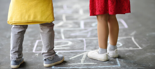Closeup of little boy and girl legs and hop scotch drawn on asphalt. Child playing hopscotch game...