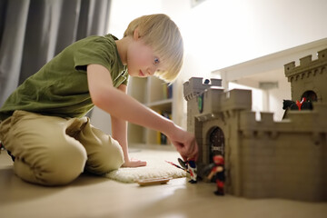 Little child is playing with toy prototype Medieval Castle. Knights and battles - favorite game for...
