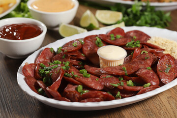 Portion of pepperoni sausage with lemon. Lettuce, green onion, ketchup and mayonnaise