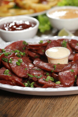 Portion of pepperoni sausage with lemon. Lettuce, green onion, ketchup and mayonnaise