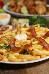 Portion of french fries with bacon. Lettuce, green onion, tomato, ketchup and mayonnaise