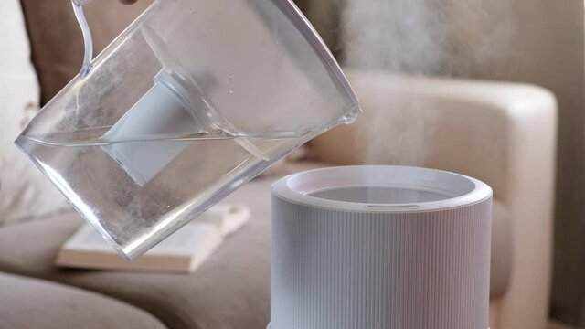 Woman pouring water from the filter to air humidifier, aroma oil diffuser at home. Improving the comfort of living in a house, Improving the well-being. Ultrasonic steam technology.