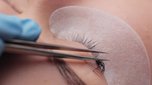 Eyelash extension procedure. The working process of professional beauty master lengthening female lashes. Fake eyelashes. Eyelashes extensions close up. Makeup artist and client in beauty salon