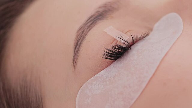 Eyelash extension procedure. The working process of professional beauty master lengthening female lashes. Fake eyelashes. Eyelashes extensions close up. Makeup artist and client in beauty salon