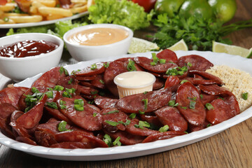Portion of pepperoni sausage with lemon. Lettuce, green onion, ketchup and mayonnaise
