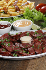 Portion of pepperoni sausage with lemon. Lettuce, green onion, ketchup and mayonnaise
