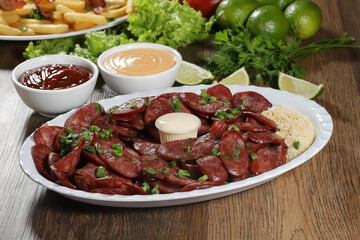 Portion of pepperoni sausage with lemon. Lettuce, green onion, ketchup and mayonnaise