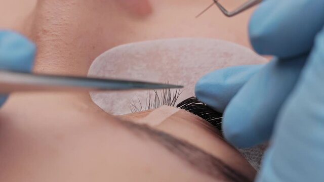 Eyelash extension procedure. The working process of professional beauty master lengthening female lashes. Fake eyelashes. Eyelashes extensions close up. Makeup artist and client in beauty salon