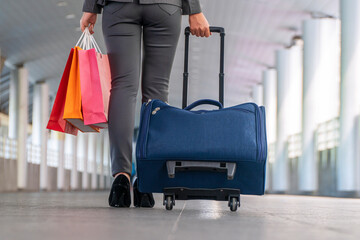 Fototapeta na wymiar Back of young woman with luggage holding color shopping bag in her hands while walking in the walkway at city. Travel trip and shopaholic concept.