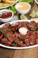 Portion of pepperoni sausage with lemon. Lettuce, green onion, ketchup and mayonnaise