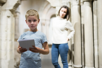 Attentive school boy exploring artworks in modern museum, woman standing on background