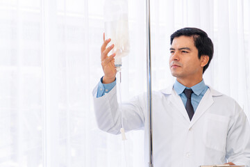 Professional doctor wear white coat uniform checking saline bag for patient at hospital room. Physician handsome young man care drip fluid saline bottle. Health care concept.